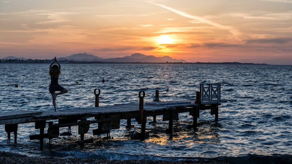 Woman performing a tranquil yoga pose on a pier near water.